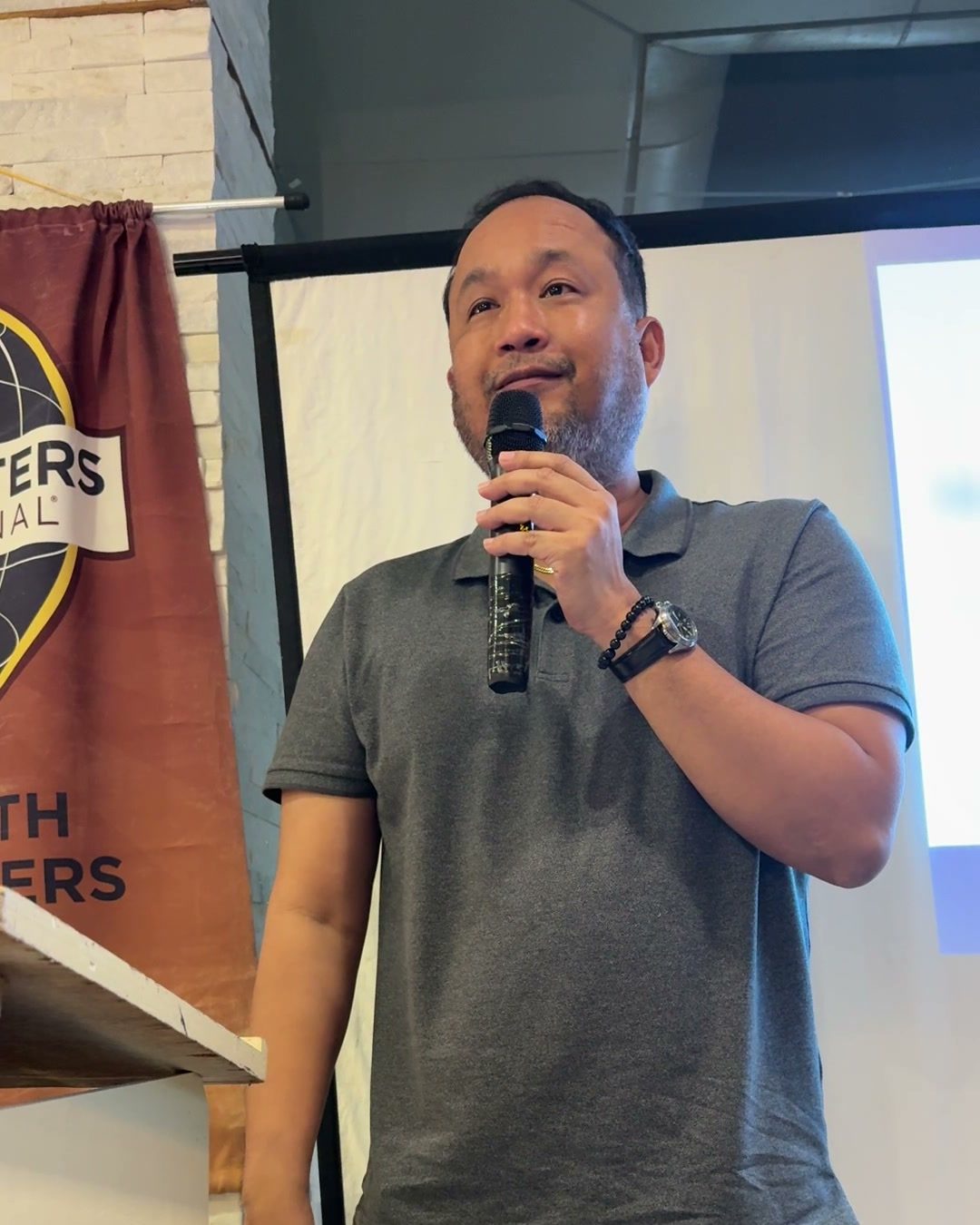 Alfred Reloj speaking with a microphone in front of the Toastmasters banner